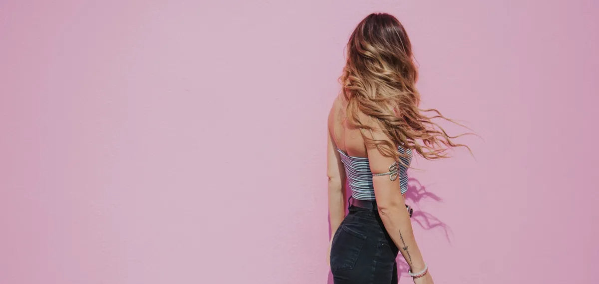 Woman with long brunette waves and caramel highlights against a pink wall